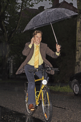 Man som cyklar med mobilen i ena handen och ett paraply i den andra